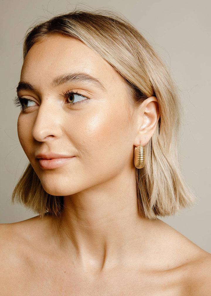 Close-up side-facing portrait of a model wearing Vincent Rowen textured gold-tone earrings