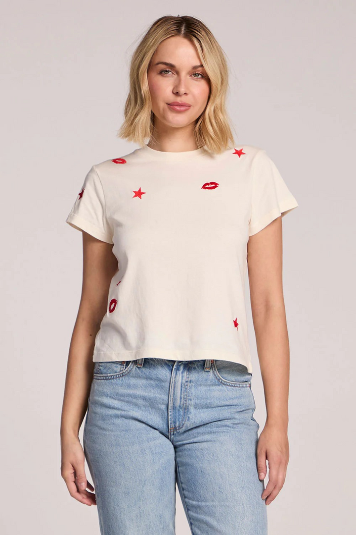 Woman wearing a cream t-shirt with red accents and blue jeans on a plain background