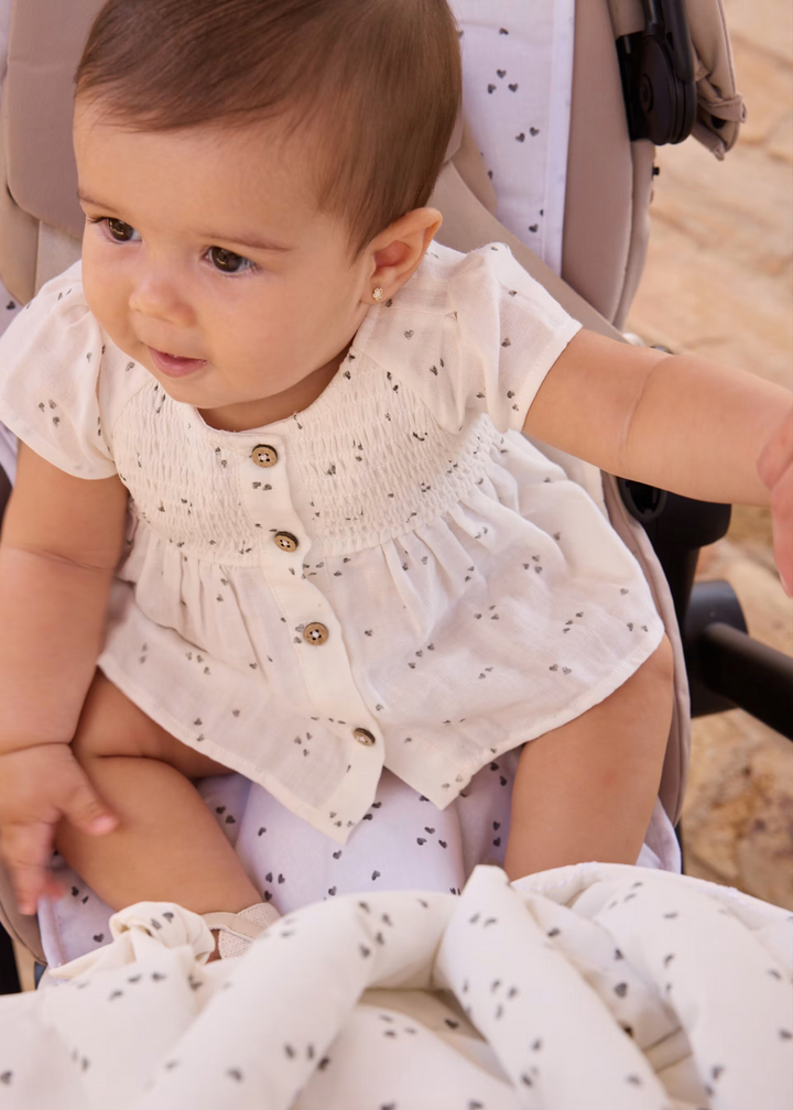 Baby in a stroller wearing a white outfit with small patterns.