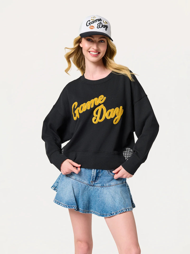 Woman wearing a black 'Game Day' sweatshirt, denim skirt, and cap on a white background