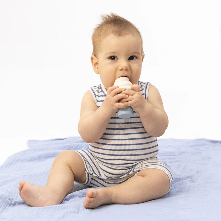 Baby in a striped outfit holding a white object on a light blue blanket