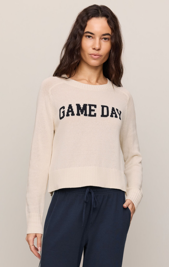 Woman wearing a beige sweater with 'GAME DAY' text on a plain background