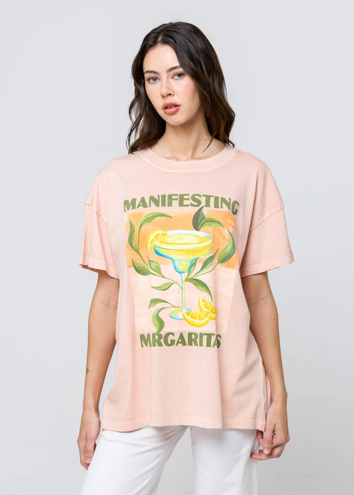 Woman wearing a pink t-shirt with a graphic design and text on a light gray background margaritas cocktails