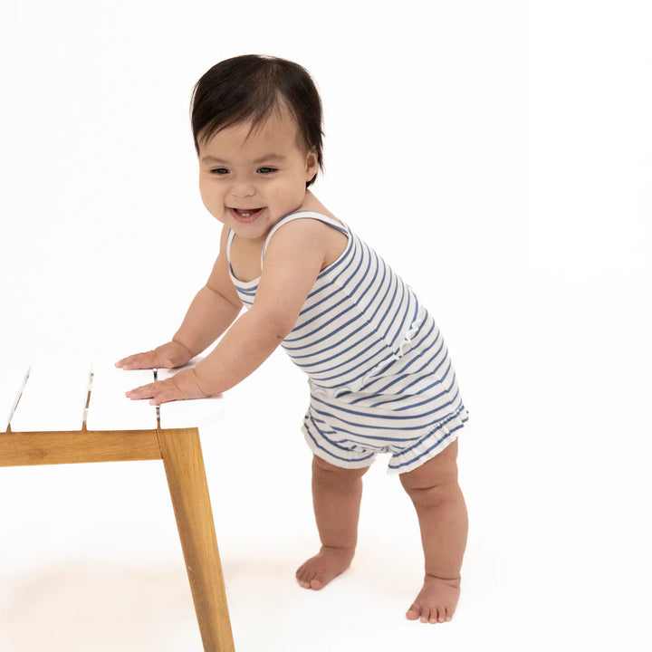 Baby in a striped outfit standing next to a wooden table on a white background