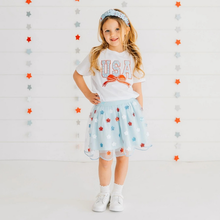 Young girl wearing a 'USA' t-shirt and star-patterned skirt against a star-patterned background
4th of July