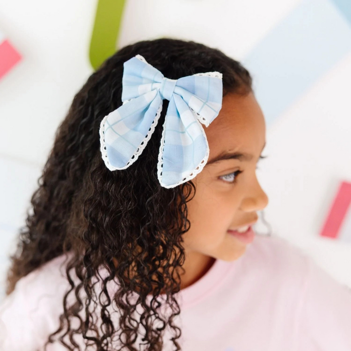 Girl with curly hair wearing a large blue bow in her hair against a colorful background