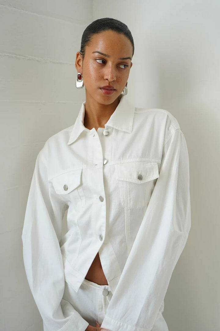 Woman wearing a white denim jacket against a plain background