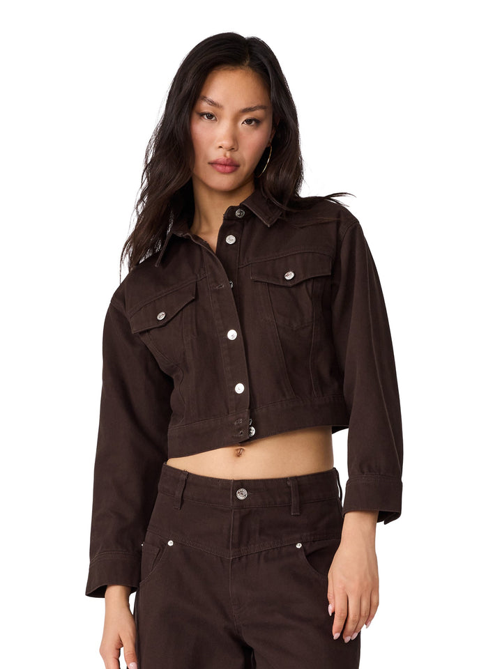 A model wearing a dark brown cropped denim jacket and matching wide-leg denim pants, paired with snakeskin-patterned heels, against a plain white background.