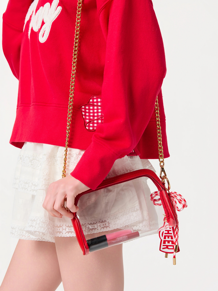 Person wearing a red hoodie and white skirt holding a clear handbag with red accents.