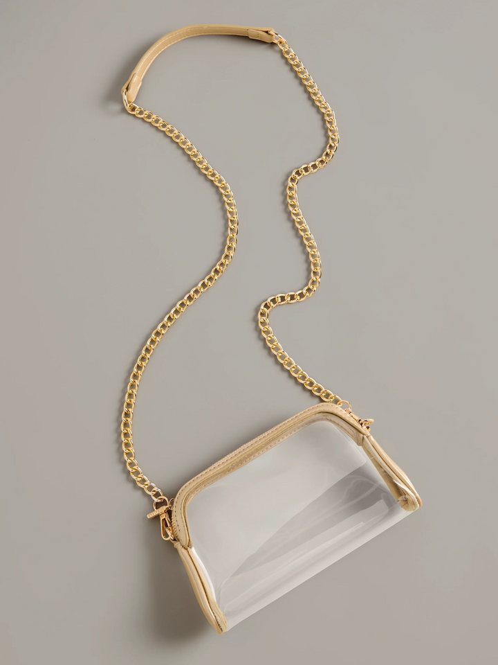 A clear plastic crossbody bag with a gold-tone chain strap and gold-tone trim, shown on a neutral gray background.