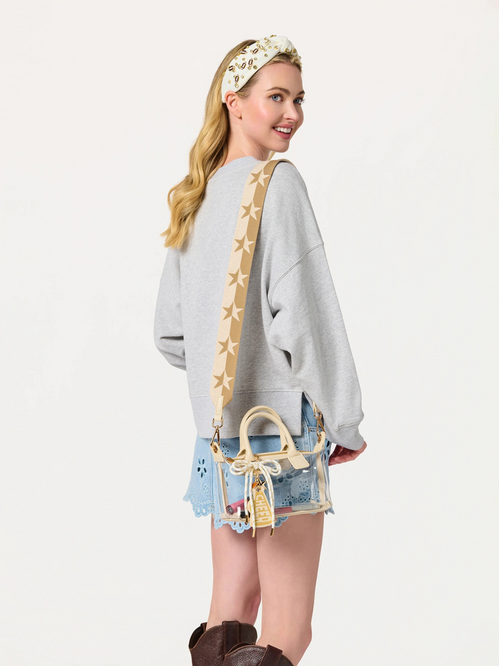 Woman wearing a gray sweatshirt with a star-patterned strap, denim skirt, and brown boots on a white background.