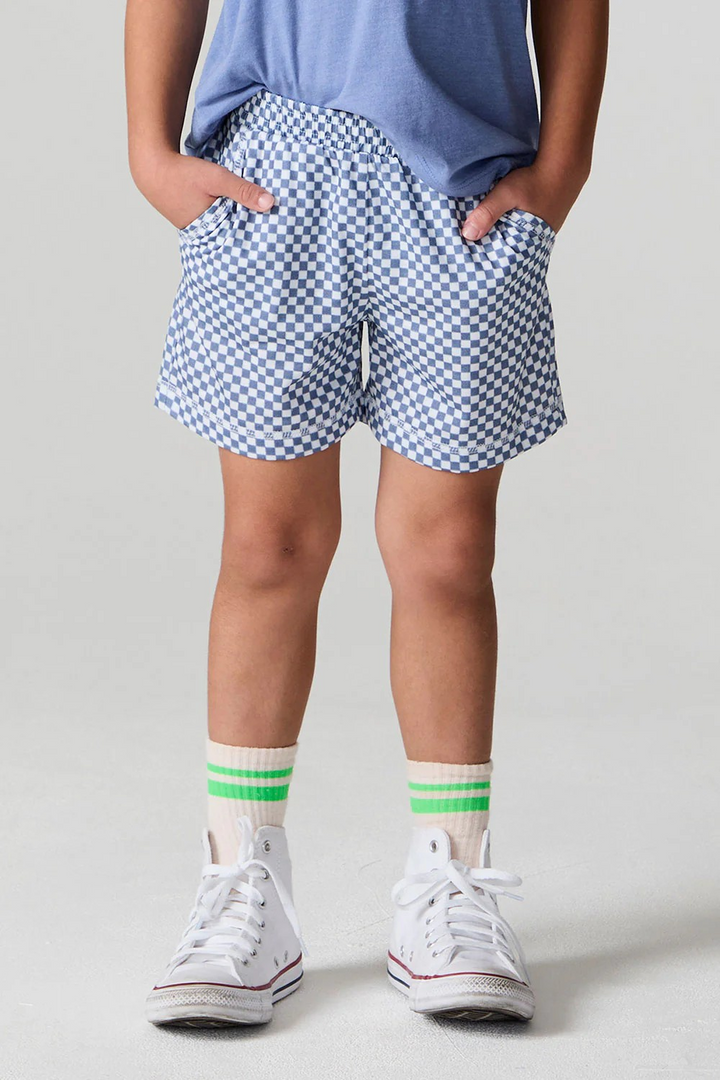 little boy wearing blue checkered shorts and white sneakers with green accents on a plain background