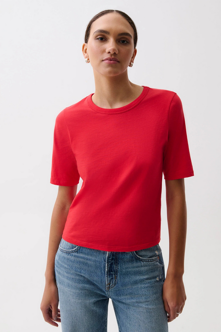 A woman modeling a bright red short-sleeve crewneck t-shirt paired with blue jeans, photographed against a clean white studio background. Pistola Melika