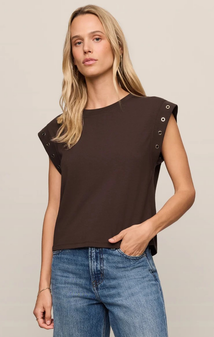 Woman wearing a brown sleeveless top with grommet details on a beige background