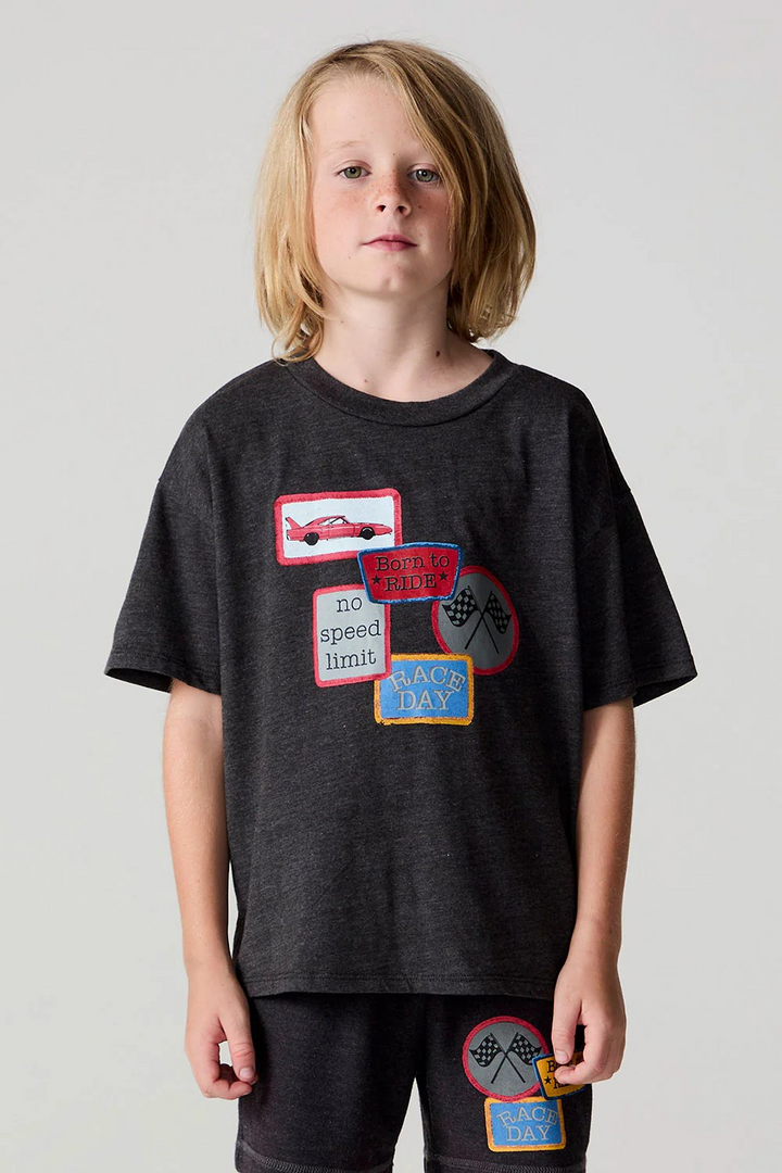 Child wearing a black t-shirt with colorful patches on a plain background